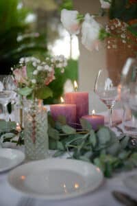 Centre de table élégant avec bougies roses, fleurs blanches et eucalyptus pour un mariage romantique.